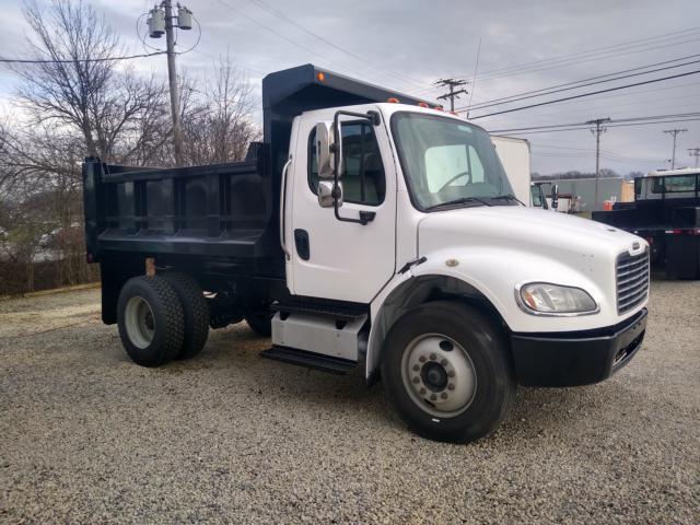 2013 Freightliner M2 dump truck with white cab and dark dump bed. Side view shows front wheel, dual rear wheels, and steps. No visible text other than generic model features.