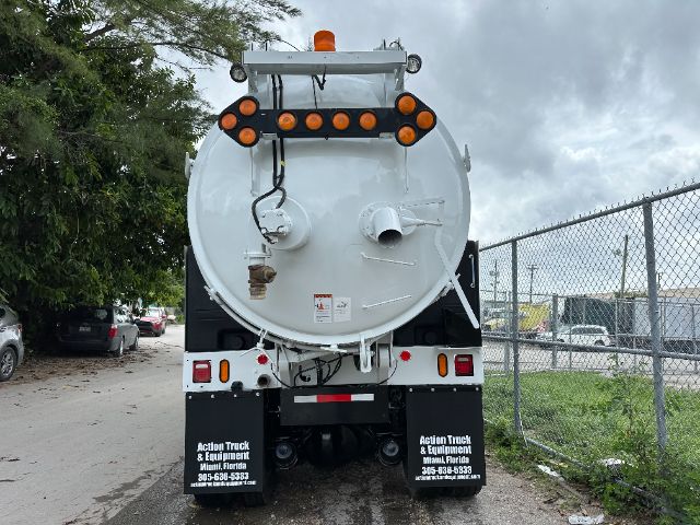 Back of a white Peterbilt vacuum truck with circular tanker, multiple orange lights, and wiring harnesses visible.