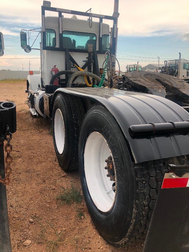 Kenworth T800 truck chassis with dual rear wheels and tank-like fuel/auxiliary components. Visible tires, wheels, and cab area with some hoses and equipment in yard.