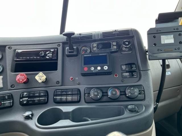 Dashboard of a Freightliner Cascadia truck showing instrument cluster, control knobs, vents, and a WARNER device mounted on the dash.