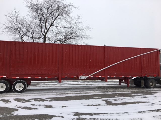 Scrap gondola trailer showing long red container on tandem axle with a diagonal support brace.