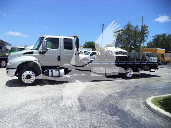 Tow truck with a long flatbed attached, chrome mirrors, dual rear wheels, and a gray cabin; clear blue sky in the background.