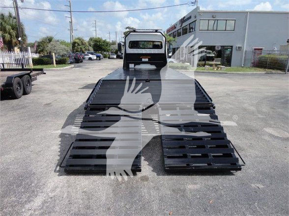 Freightliner truck with two fold-down bed ramps in a dealership lot.