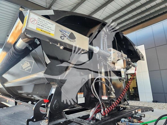 Industrial dump trailer in a showroom with hydraulic arms and warning labels visible.