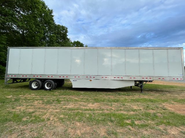 Exterior side view of a gray 53 ft Vanguard trailer with landing gear and dual rear axles on grass. Clear sky and trees in background.