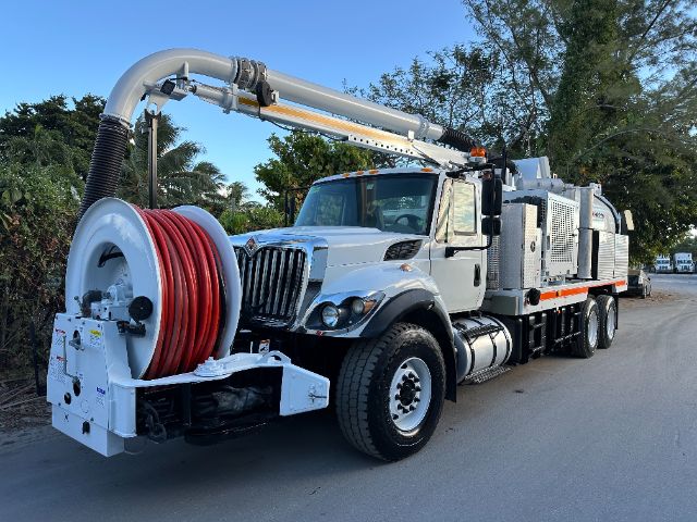 International 7400 vacuum truck with large hose reel and reel hose on a street, front grille, dual rear axles, and mounted equipment compartments.