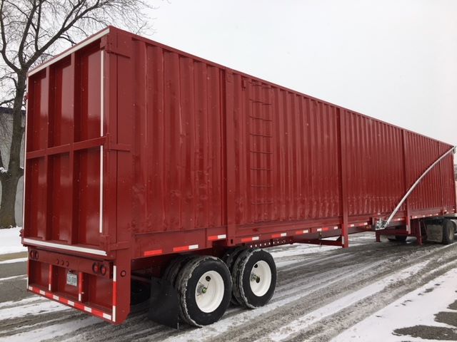 Red scrap gondola trailer with dual rear axles and white wheels on a snow-covered road.