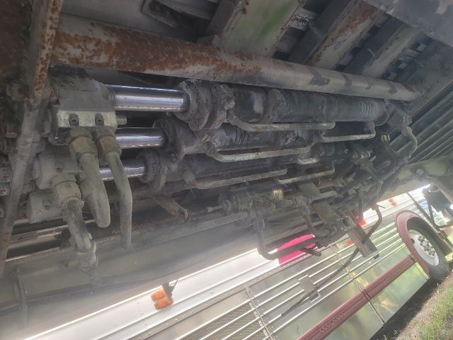 Underbelly of a walking floor trailer showing hydraulic cylinders and linkage with rust and grime.