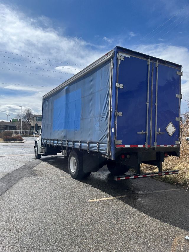 Freightliner M2 106 box truck with blue curtain-side cargo area, rear double doors, white cab, in-service on pavement.