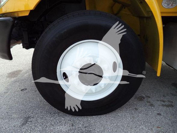 Wheel and tire of a yellow box truck, close-up view showing rim and part of the fender; watermark overlay with birds in flight is visible.