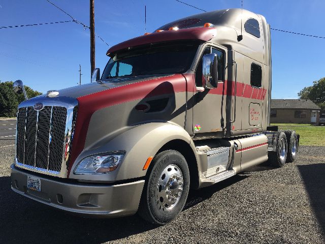 Peterbilt 578 truck in tan and maroon, front three-quarter view, cab with sleeper, chrome grille, dual rear axles, truck parked on gravel.
