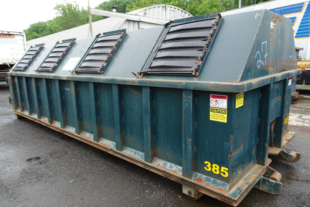 Wastequip 20 yd dumpster in blue with rear wheels and safety labels, numbered 385, side view showing top lids and rusted edges.