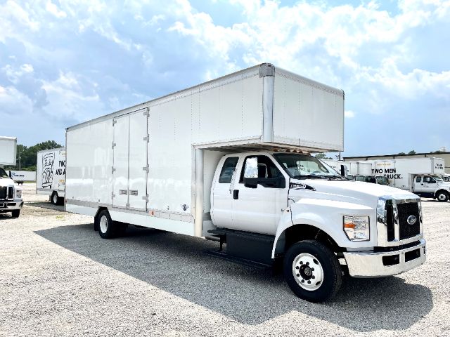 White 2025 Ford F650 box truck with a large cargo box, front grille and cab visible, parked on gravel.