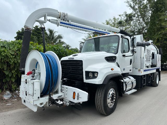 Truck equipped with vacuum system, white Freightliner 114SD with large hose reel and elevated boom, front grille, dual rear axles, and vacuum mounting unit.