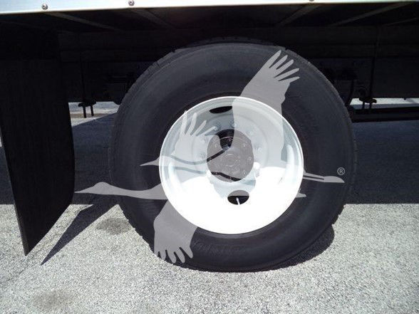 Truck axle and wheel showing tire and white rim under trailer