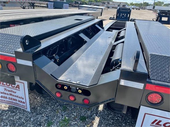 Lowboy trailer deck surface with hydraulic ramps and storage compartments showing metal diamond plate textures and rear lighting.