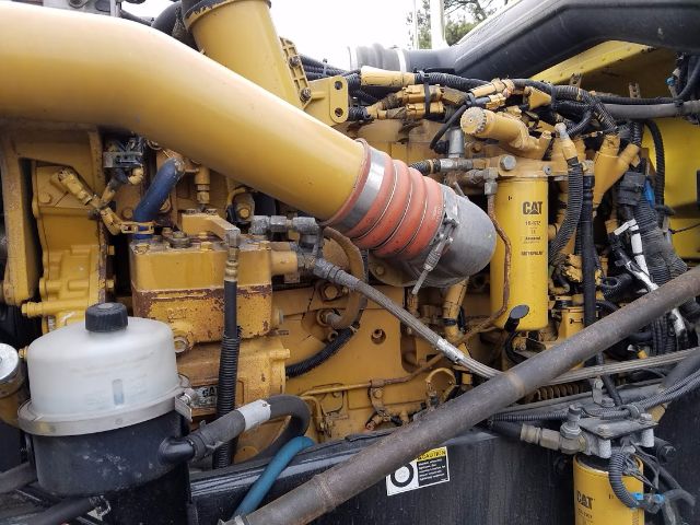 Peterbilt 389 engine bay showing large yellow engine with CAT branding and various hoses and hoses; white reservoir and black/rusty components.