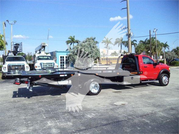 Ram 5500 tow truck with a flatbed trailer attached, red cab, black flatbed, utility equipment in background.
