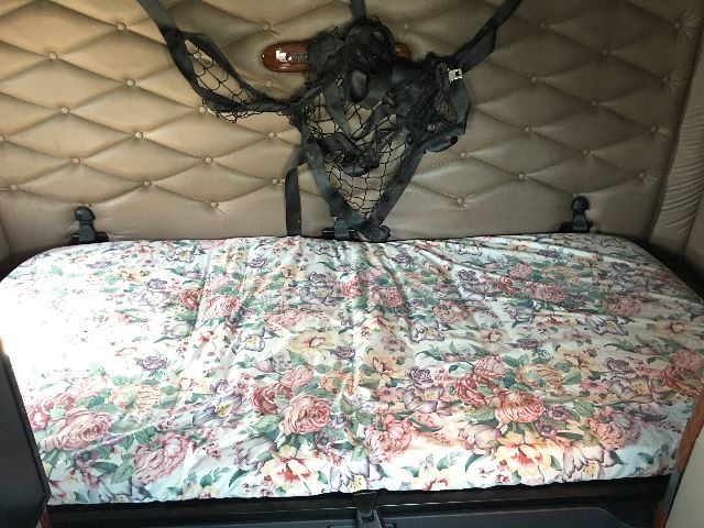 Cab interior showing a floral-patterned sleeper couch with quilted tan padded walls and cargo netting.