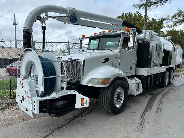 Peterbilt 340 vacuum service truck with large reel and hose assembly on front, long dual rear axles, silver cab and vehicle-mounted equipment.