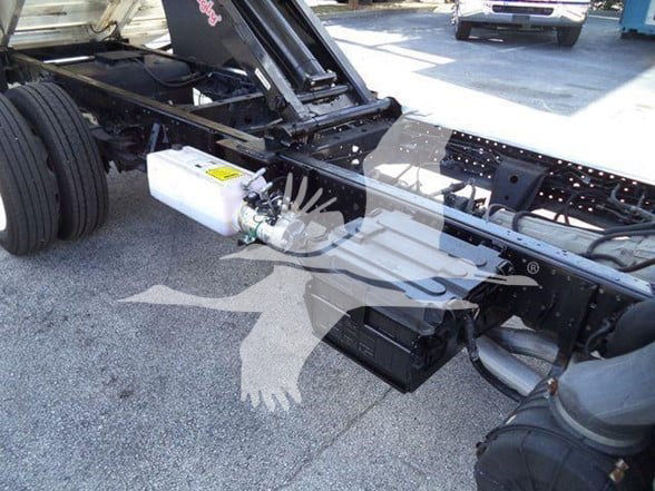 Isuzu NPR HD chassis showing brake reservoir (white container) mounted near frame with hoses and a battery nearby.