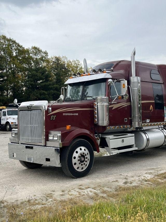 Tractor unit in maroon with chrome accents and vertical exhaust stacks; front grille and bumper; large round fuel tanks; side steps and mirrors; Detroit 14L badging visible.