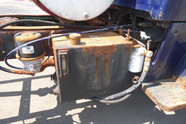 Tractor unit cab and chassis with rusted black metal reservoir and hoses, hydraulic pump, filter, and mounting brackets visible.