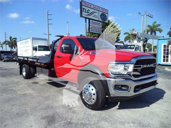 Ram 5500 tow truck in red cab with black flatbed, front grille RAM badge, dealership lot in background.