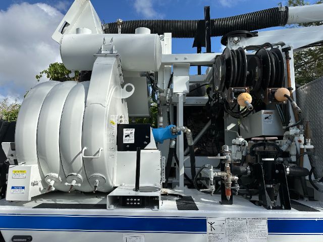 Forklift-style vacuum truck side view with reel hoses and blue gloves visible on controls.