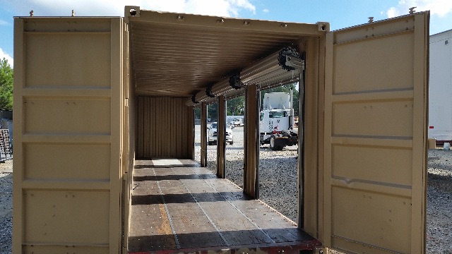 Interior of a beige/trailer container with roll-up material along the ceiling and vertical support posts, open double doors, showing empty cargo space.