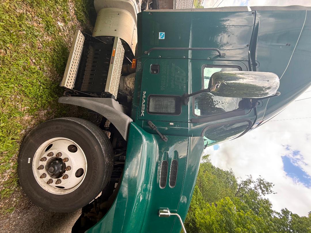 Truck cab side view showing Mack CXU 612 green exterior, large chrome mirror, front wheel, steps, and exhaust stack.