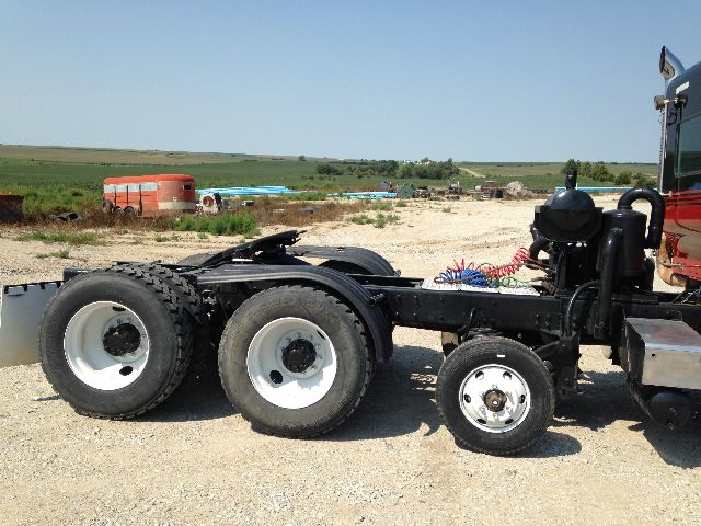 Kenworth T800 chassis with dual rear axles and exposed drive train, incomplete cab area, on dirt lot.