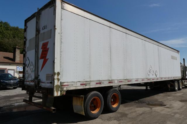 Trailer side view showing large box trailer with white exterior and orange-rimmed wheels.