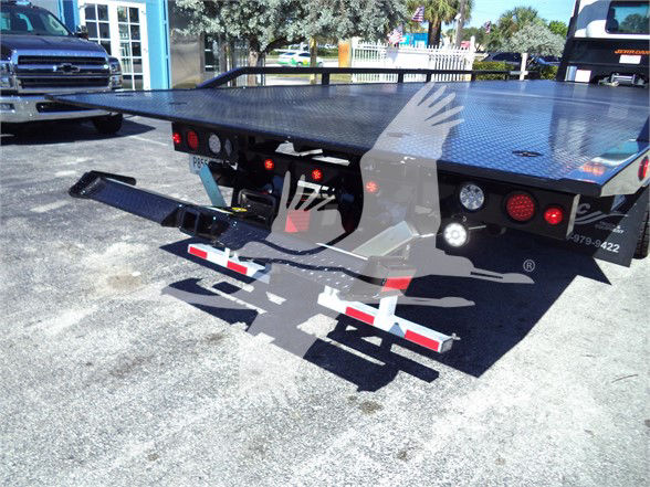 Isuzu FTR flatbed tow truck rear view with ramp lowered, diamond plate deck, dual rear lights, and a large hydraulic tow setup.