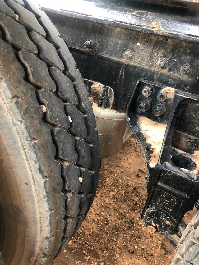Trucks trailer suspension area showing spare tire mounted near wheel, leaf spring mount, and frame with bolts.
