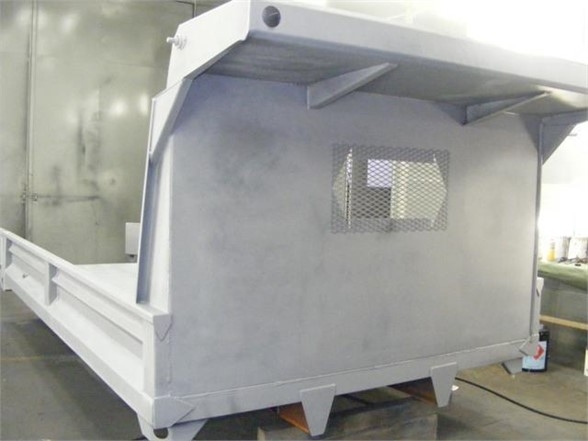 Flatbed dump body side with a perforated window and metallic gray surface; visible triangular support braces and rear skid plates.