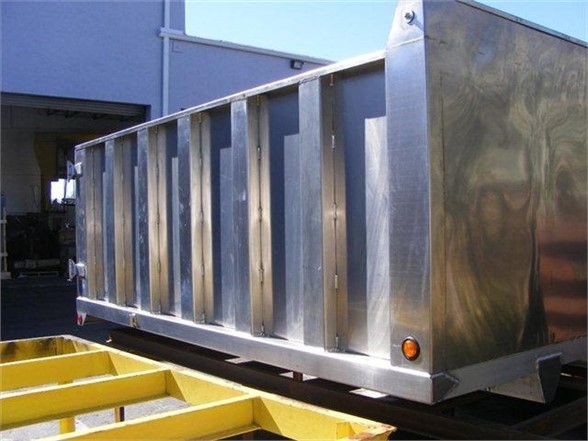 Dump body truck trailer in-site with metallic silver panel walls and reflective finish, side view showing reinforced ribs, right corner with amber marker light.