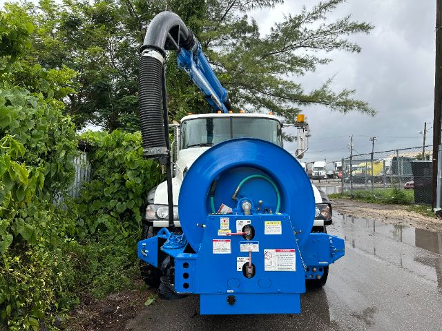 Rear view of a blue industrial vacuum truck attachment mounted on a Mack GU713 chassis, with a circular hose reel and black exhaust hose extending upward.