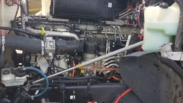 Truck engine bay showing various hoses, metal lines, and fluid reservoirs.