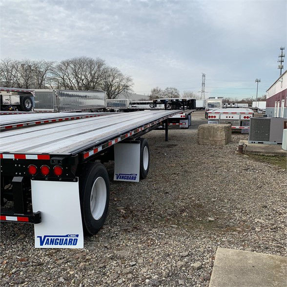A 48ft Vanguard steel flatbed trailer in a lot, showing tandem axles, white Vanguard mud flaps, and reflective tape along the edges.