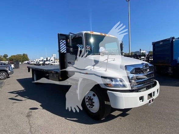 Flatbed truck in a dealership lot with white cab, black flatbed, and logo watermark. VIN and stock not visible on image.