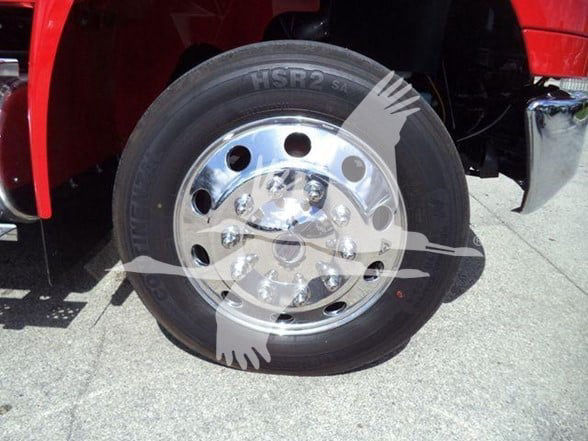 Truck wheel and tire assembly with polished chrome hub and lug nuts, mounted on a red truck fender; tire shows HSR2 marking.