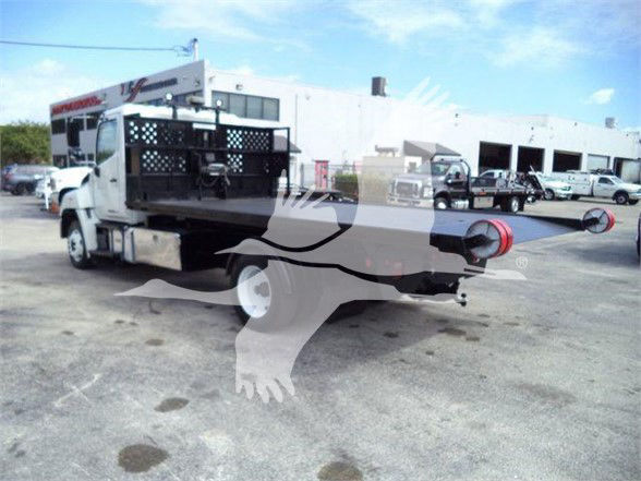 Hino 258LP hooklift truck with flatbed and extended rear stabilizers visible in a dealership lot