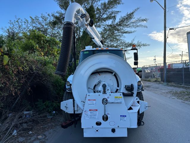 Back view of a white vacuum truck with a large circular rear equipment housing and a vacuum hose attached to an articulating boom.