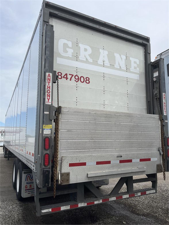 Rear of a gray grain trailer with ramp/door, GRANE lettering, red stock number 847908, chains, taillights, and reflective markers.