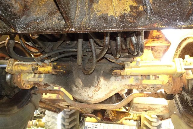 Underbelly view of a Grove RT58 crane truck showing rear axle, driveline, hydraulic lines, and yellow-painted components with signs of wear.