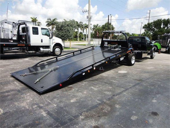 Ram 5500 SLT flatbed tow truck with long black steel flatbed and a dual-axle trailer hitch, parked on lot.