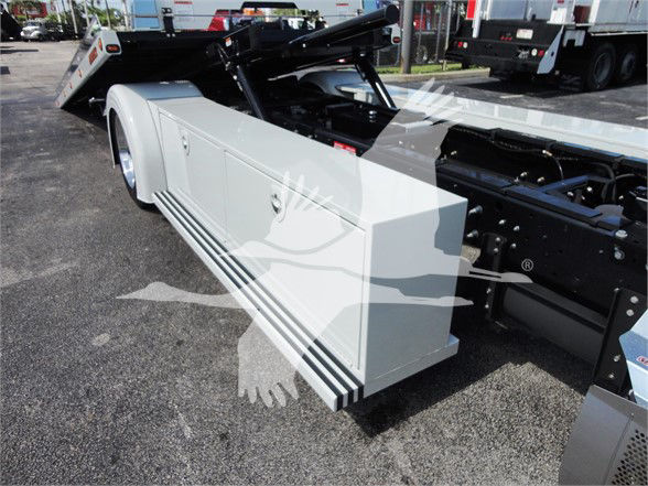 Side view of a white utility truck bed on a 2022 Hino 268A, showing the long storage box along the side and rear wheel, with hydraulic components in the chassis area.