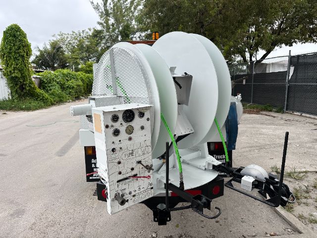 Utility truck with large spool and control panel mounted at rear, hose reel, and vacuum equipment.