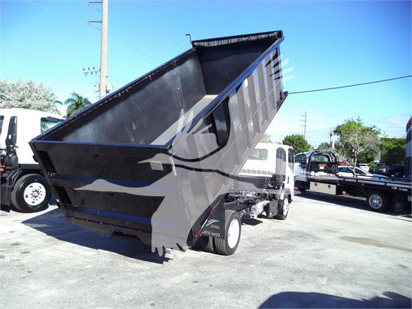 Isuzu NRR dump truck with bed raised, showcasing the cargo dump bed and chassis in an outdoor lot.